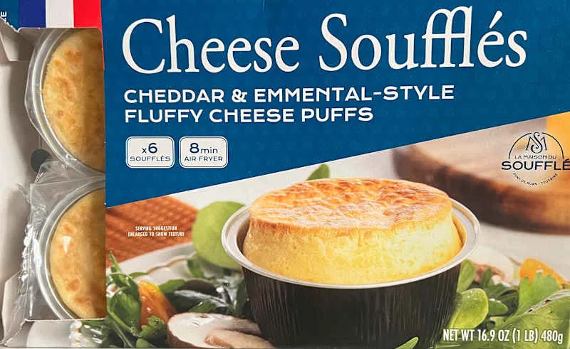 Cheese soufflés in black cups, featuring a golden top, with a serving suggestion of salad and vegetables.