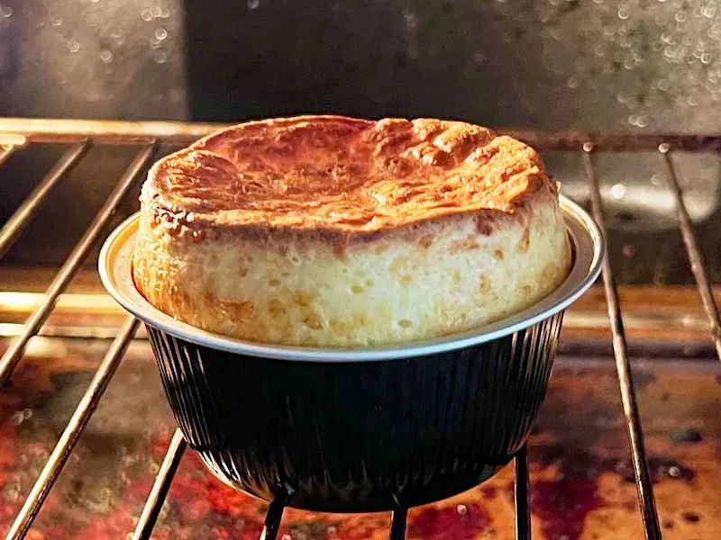 A golden-brown soufflé rising in a black baking dish inside an oven.