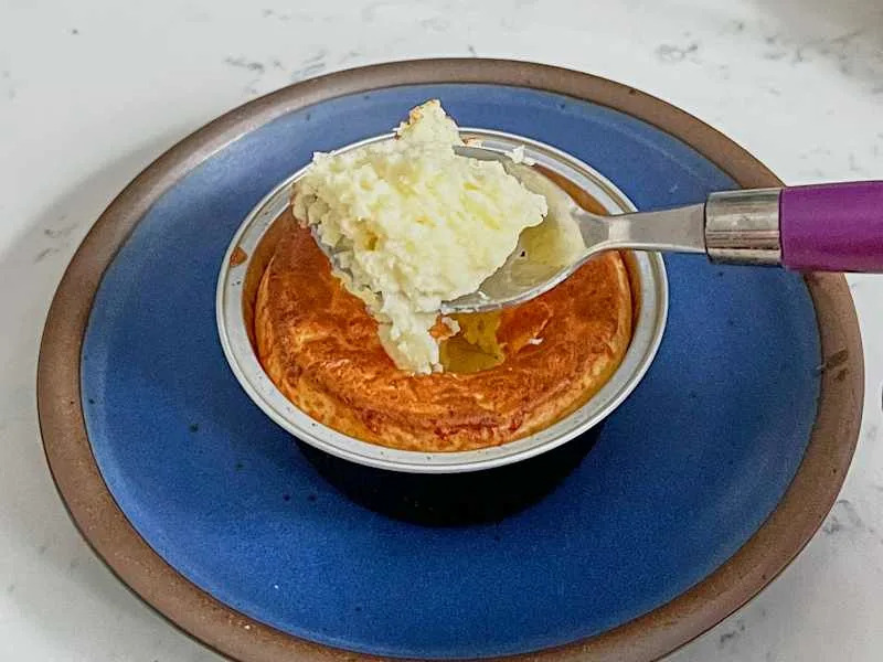 A spoonful of fluffy soufflé being lifted from a round dish on a blue plate.