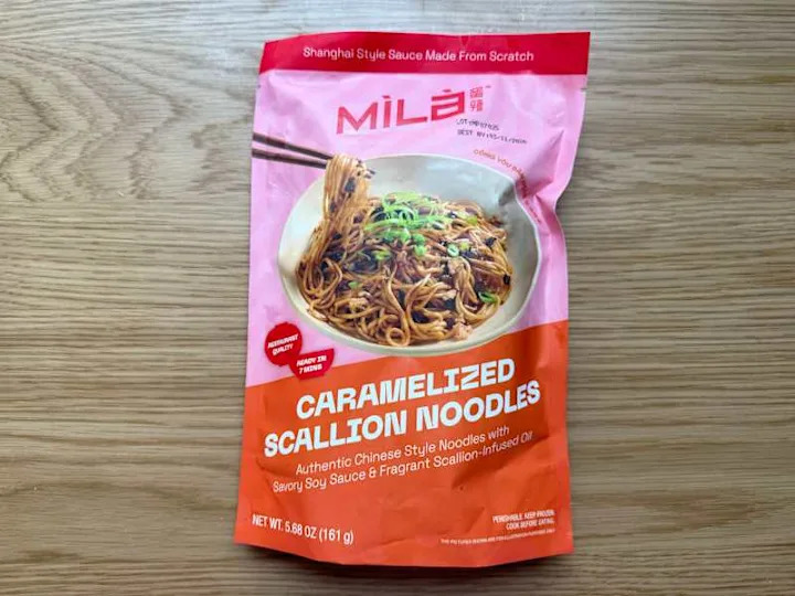 Packaging for caramelized scallion noodles featuring a bowl of noodles with green onions, chopsticks, and vibrant colors.