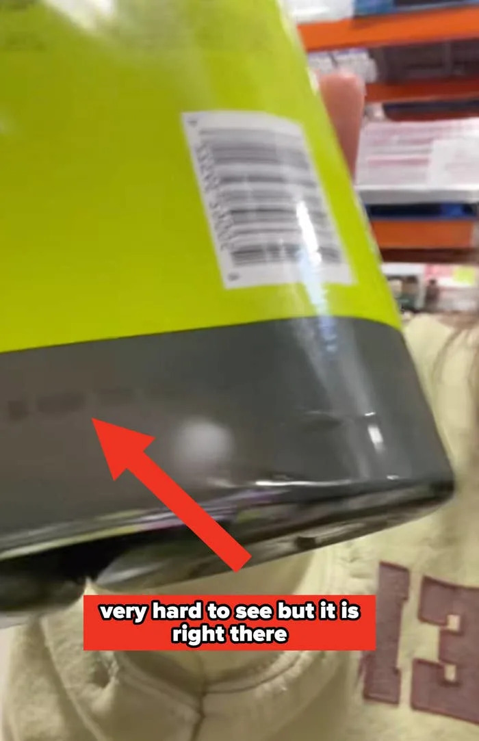 A person holds a canned food item with a dent at the bottom, showing a close-up of the barcode and label