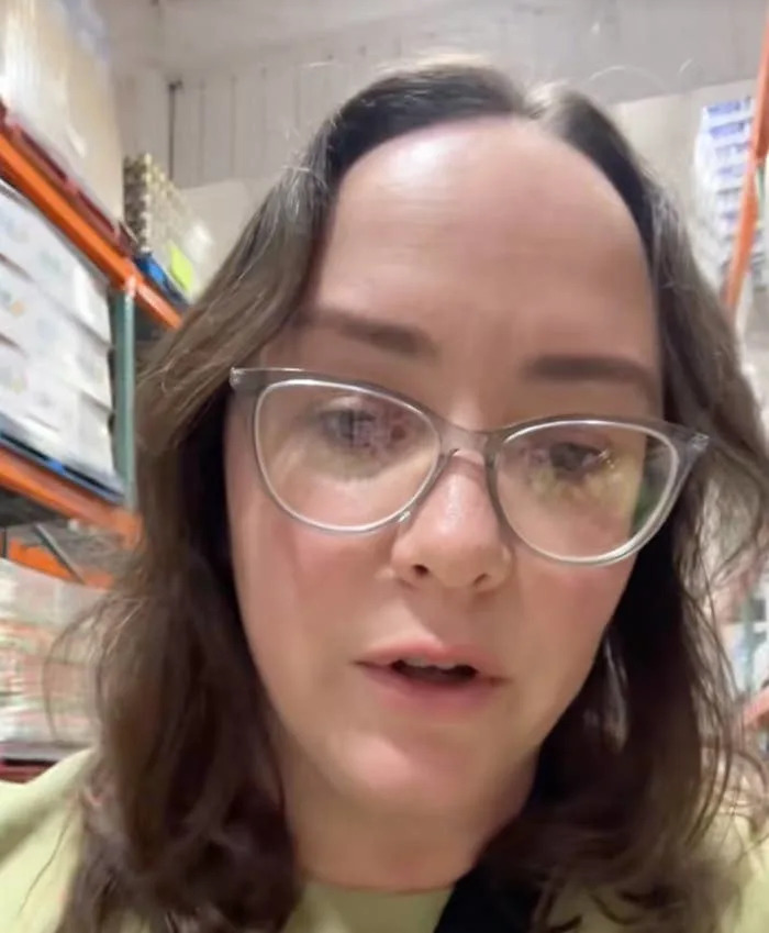 A person with glasses is speaking in a grocery store aisle. The overlaid text discusses the harvest date indicating 100% olive oil authenticity