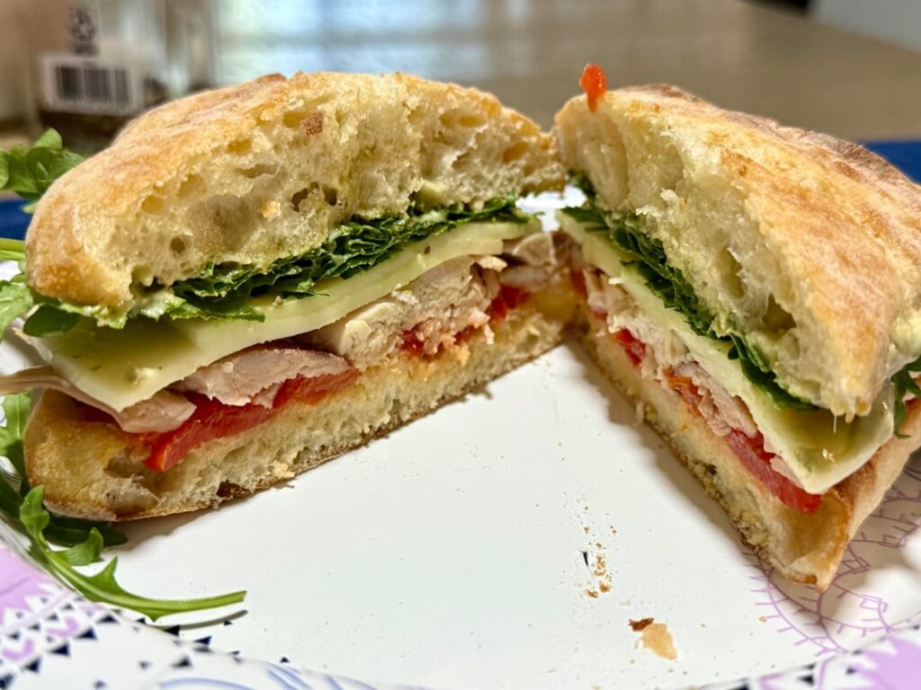 Pesto chicken sandwich with roasted red peppers, chicken thigh meat, provolone, arugula, and a pesto mayo spread.
