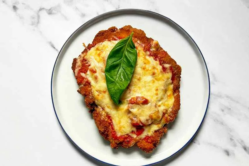 Breaded chicken cutlets topped with marinara sauce and melted cheese on a foil-lined baking sheet.