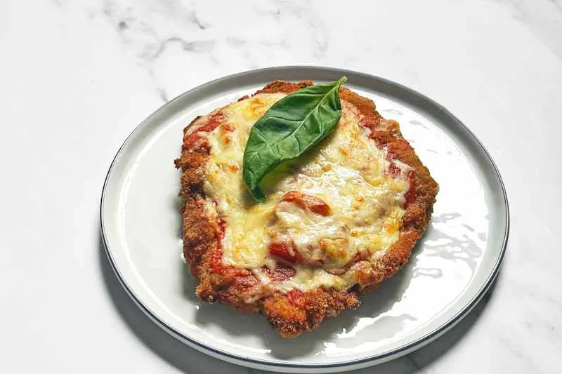Two breaded chicken cutlets topped with marinara sauce and melted cheese on a foil-lined baking sheet.