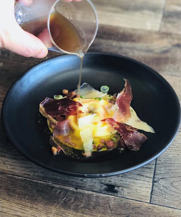 Bone broth poured over raviolo of agria and egg yolk with iberico consommÃ© and brioche crouton.