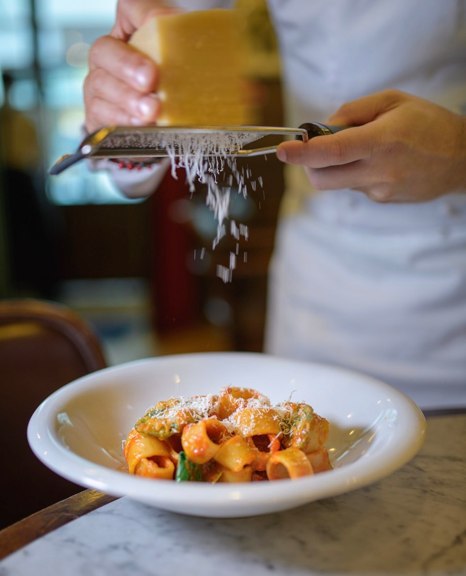 A chef grates cheese over a pasta dish.