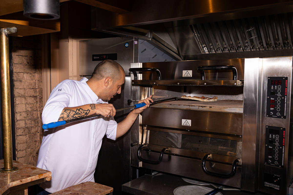 a pizza maker using a pizza paddle to check on pizzas cooking in a large pizza oven