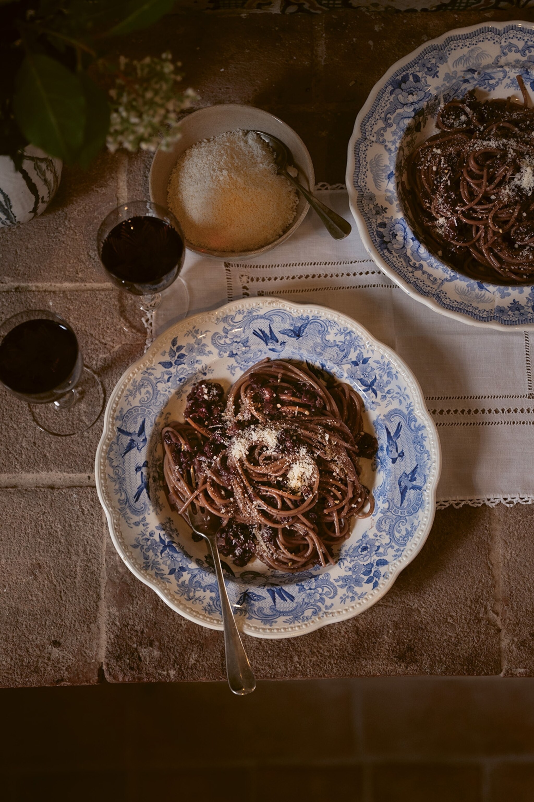 A rustic table scape with a plate of spaghetti and smashed olive sauce served with red wine.
