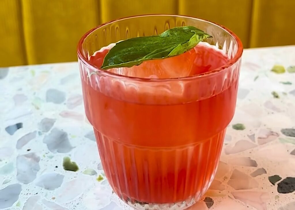 This photo shows the red-colored Pepperoni Pizza Negroni in a glass with a basil leaf.