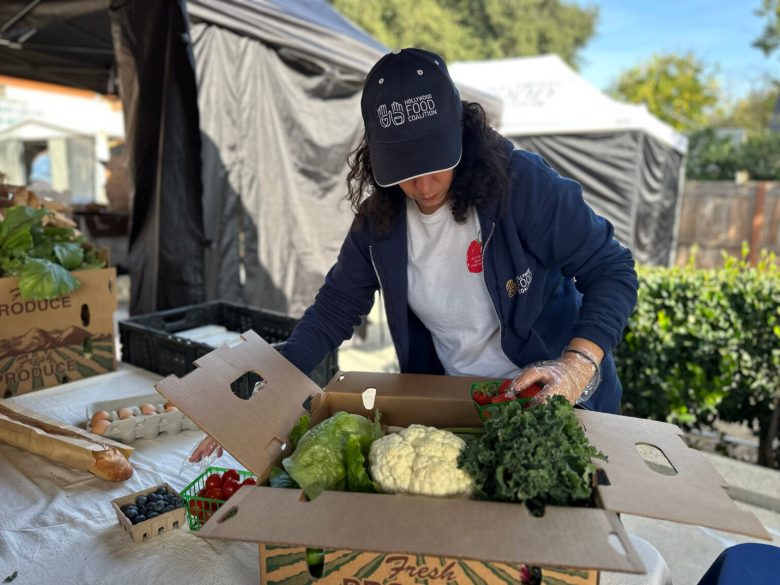 A person packs fresh produce into a box at an outdoor market stand.
