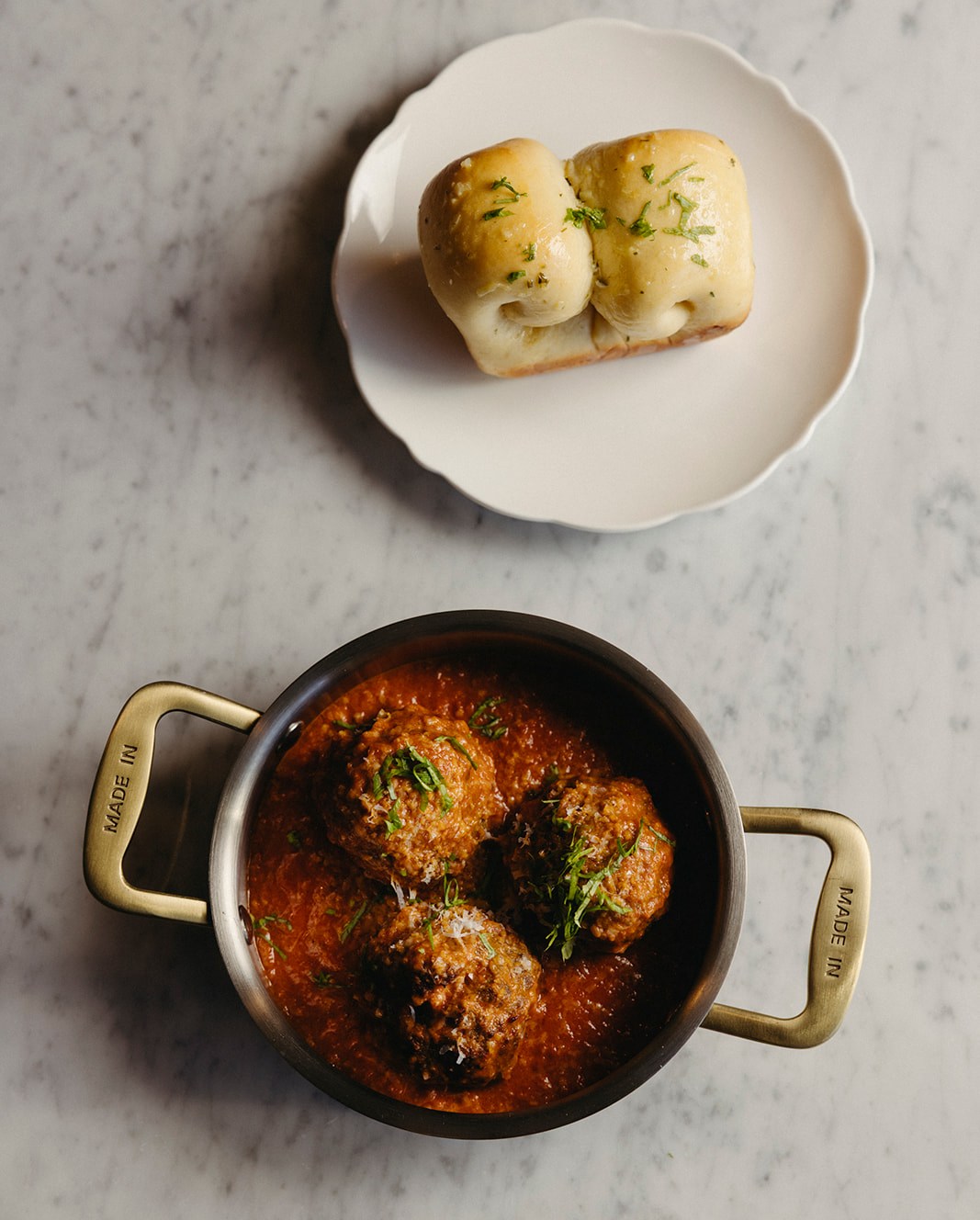 Overhead shot of meatballs in a shallow pan and a side of milk bread.
