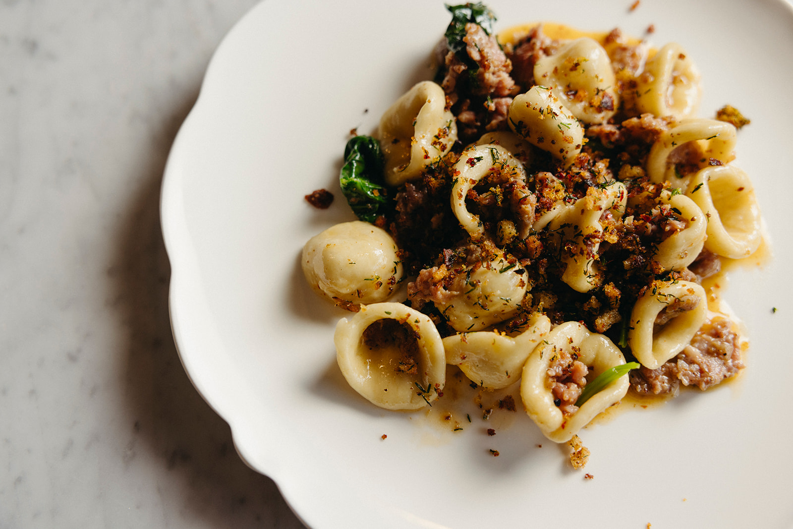 Overhead shot of orecchiette dotted with fennel and gochujang sausage on a white plate.