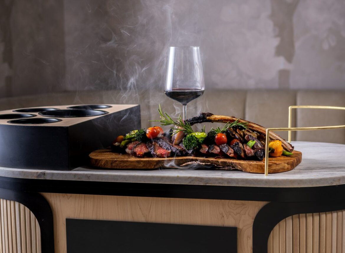 A cart topped with a platter of steak and a glass of red wine.