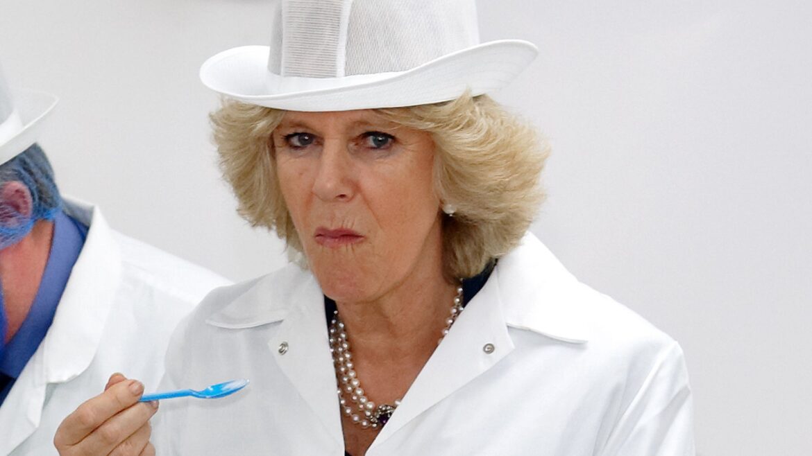 Queen Camilla wears a white coat and hat and eats something