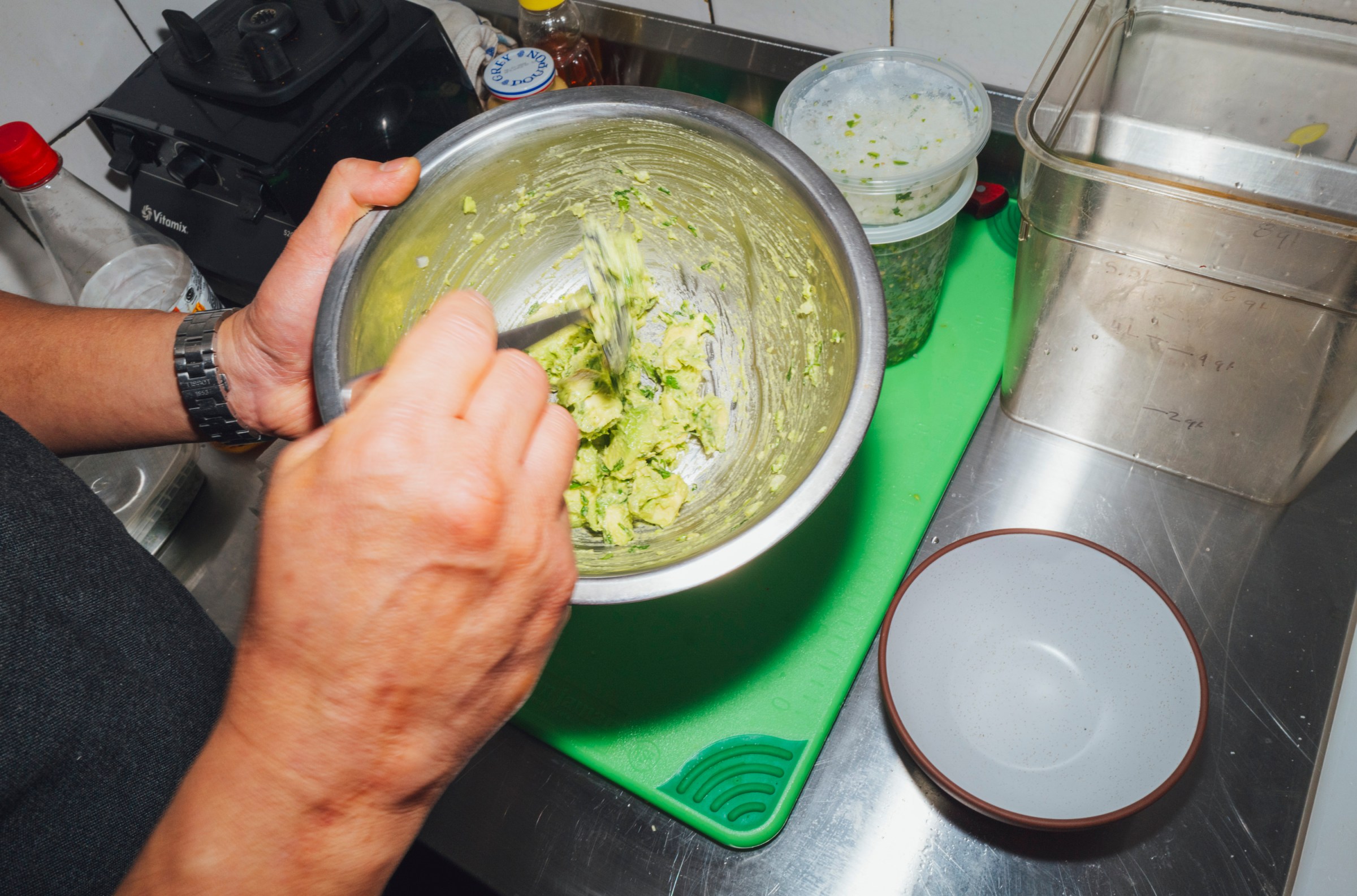 Someone mixing up guacamole in a metal bowl.