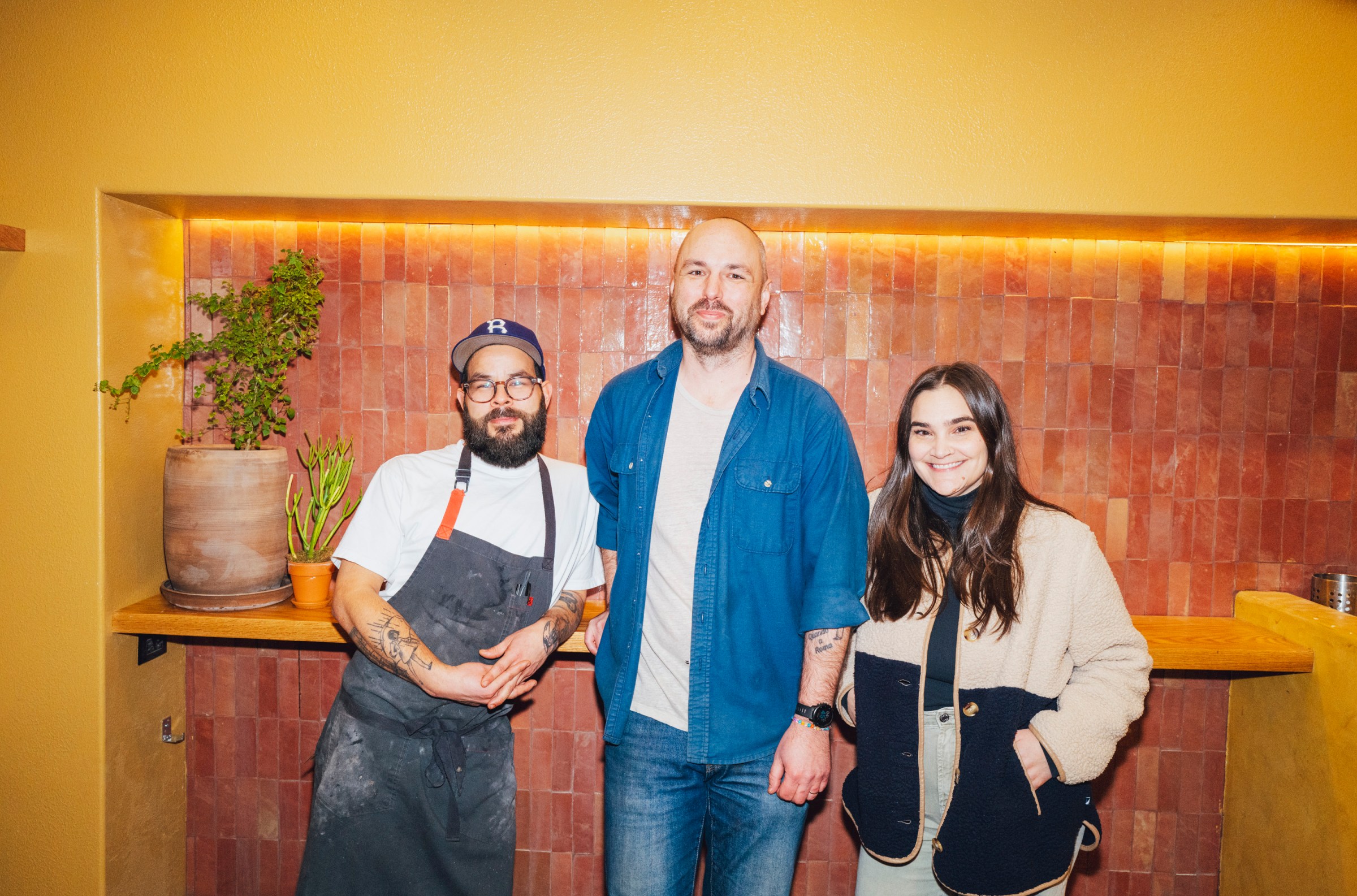 Three people posing in front of a tiled wall.