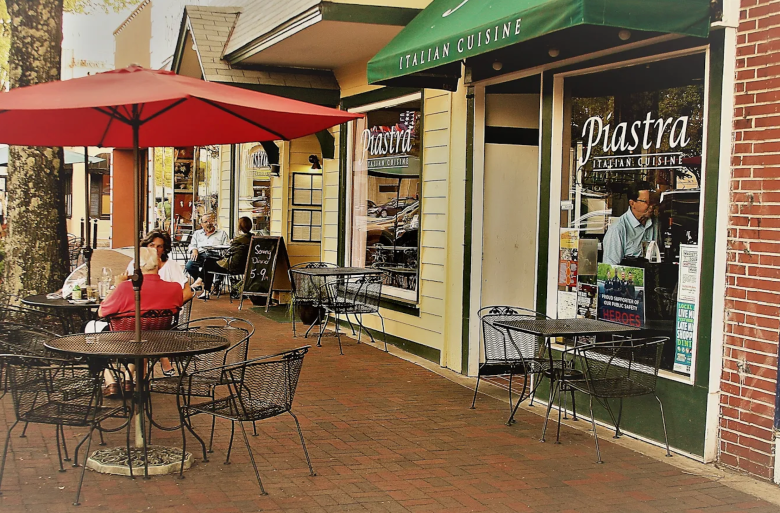 Piastra Italian restaurant on Marietta Square with an outdoor patio dining area with red umbrellas and metal tables in downtown storefront setting.
