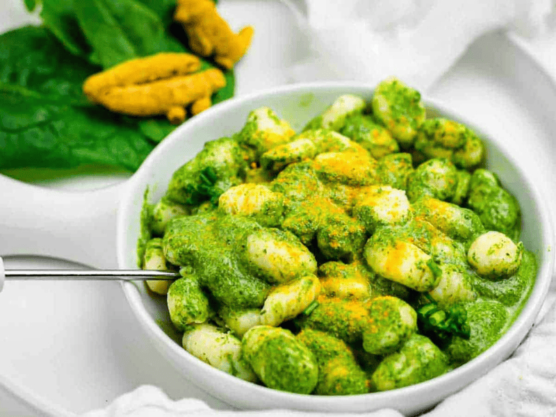 Bright green gnocchi sauce with orange turmeric powder over the gnocchi plate.