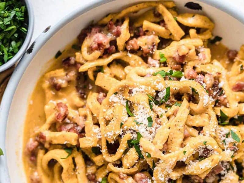 Pasta Carbonara inside a bowl with herbs and bacon.