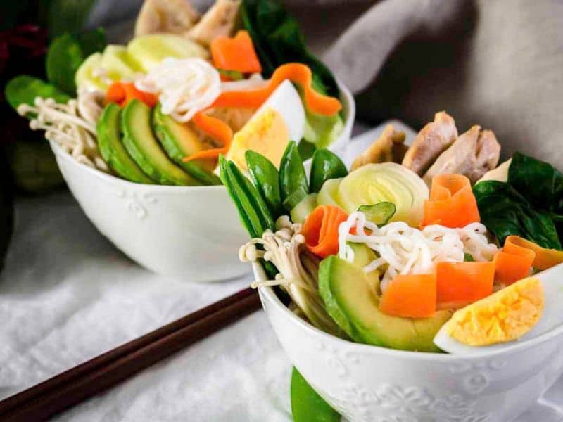 Two bowls of spicy ramen noodles with veggies on top.