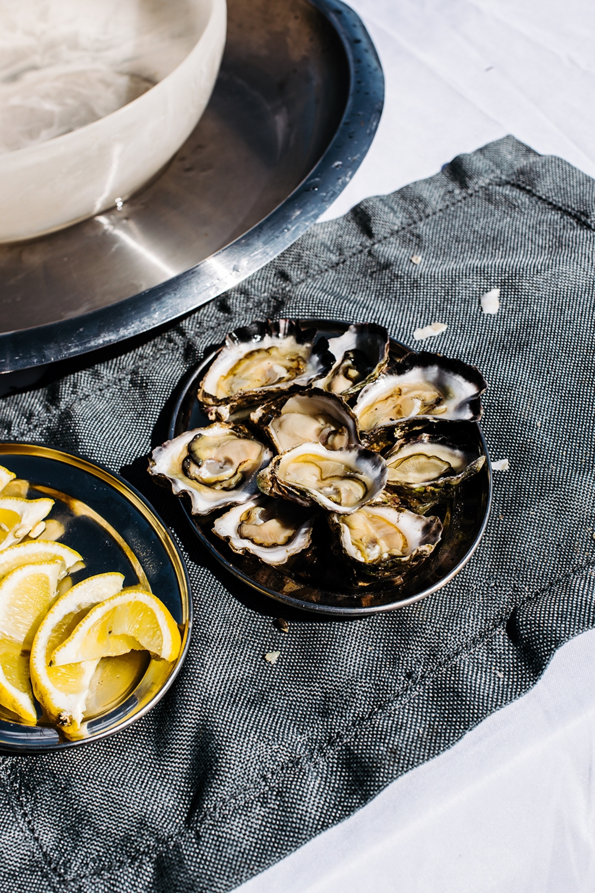 A plate of freshly shucked oysters in the sunshine with a side of lemon wedges.