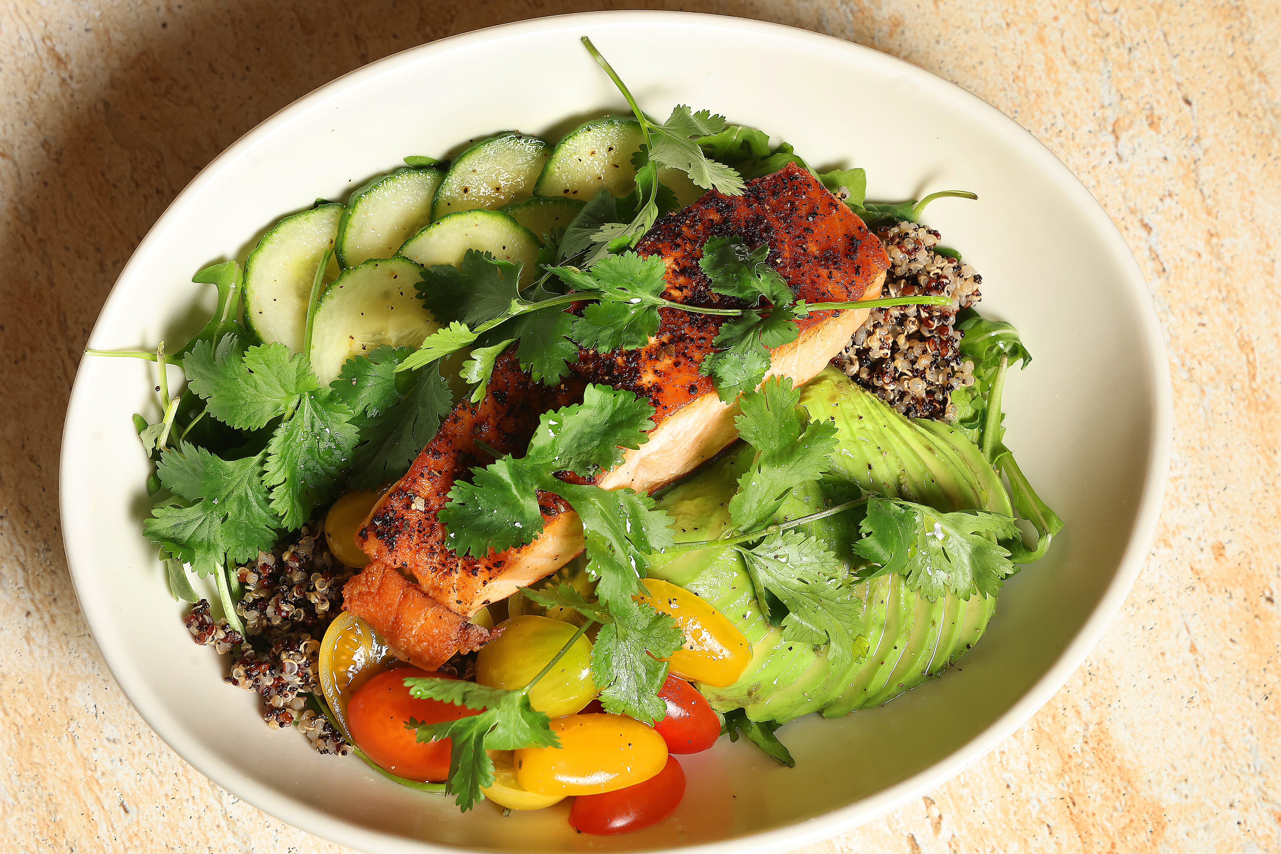 A spicy bowl featuring salmon, quinoa, arugula, avocado, cherry tomato,...