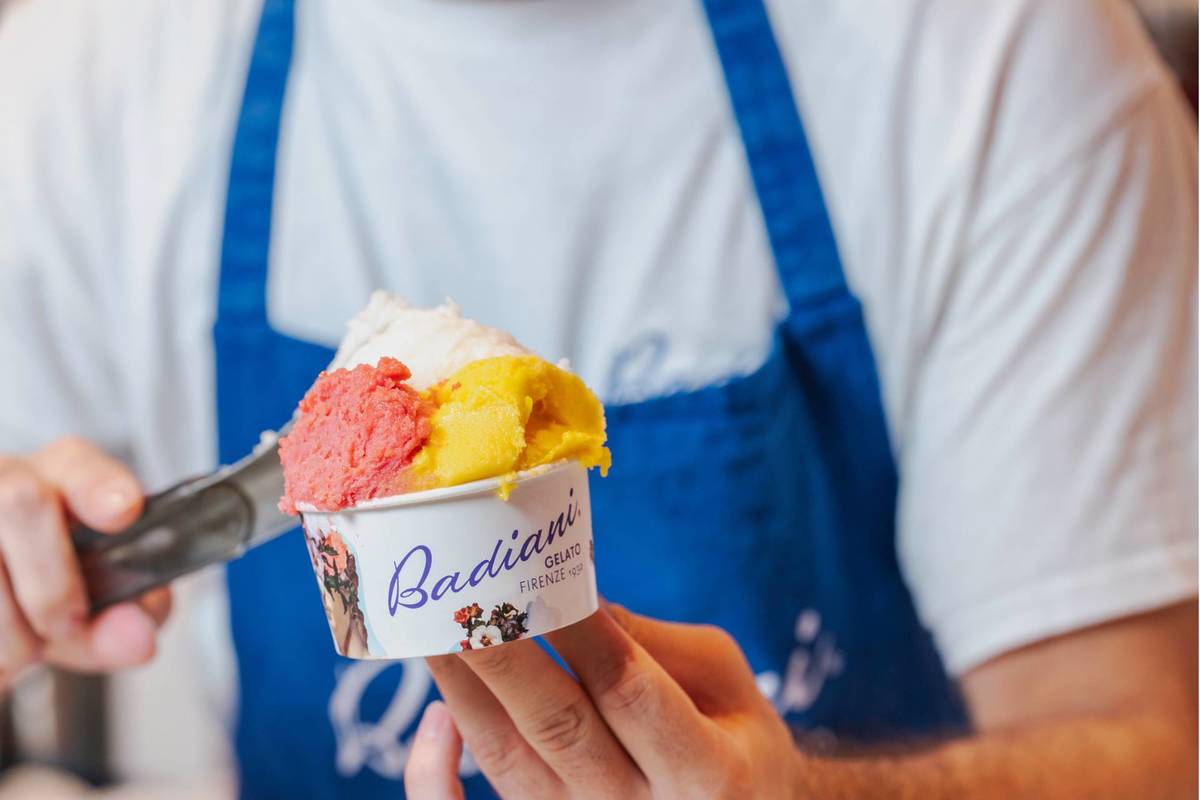 someone filling a cup with gelato in three different flavours