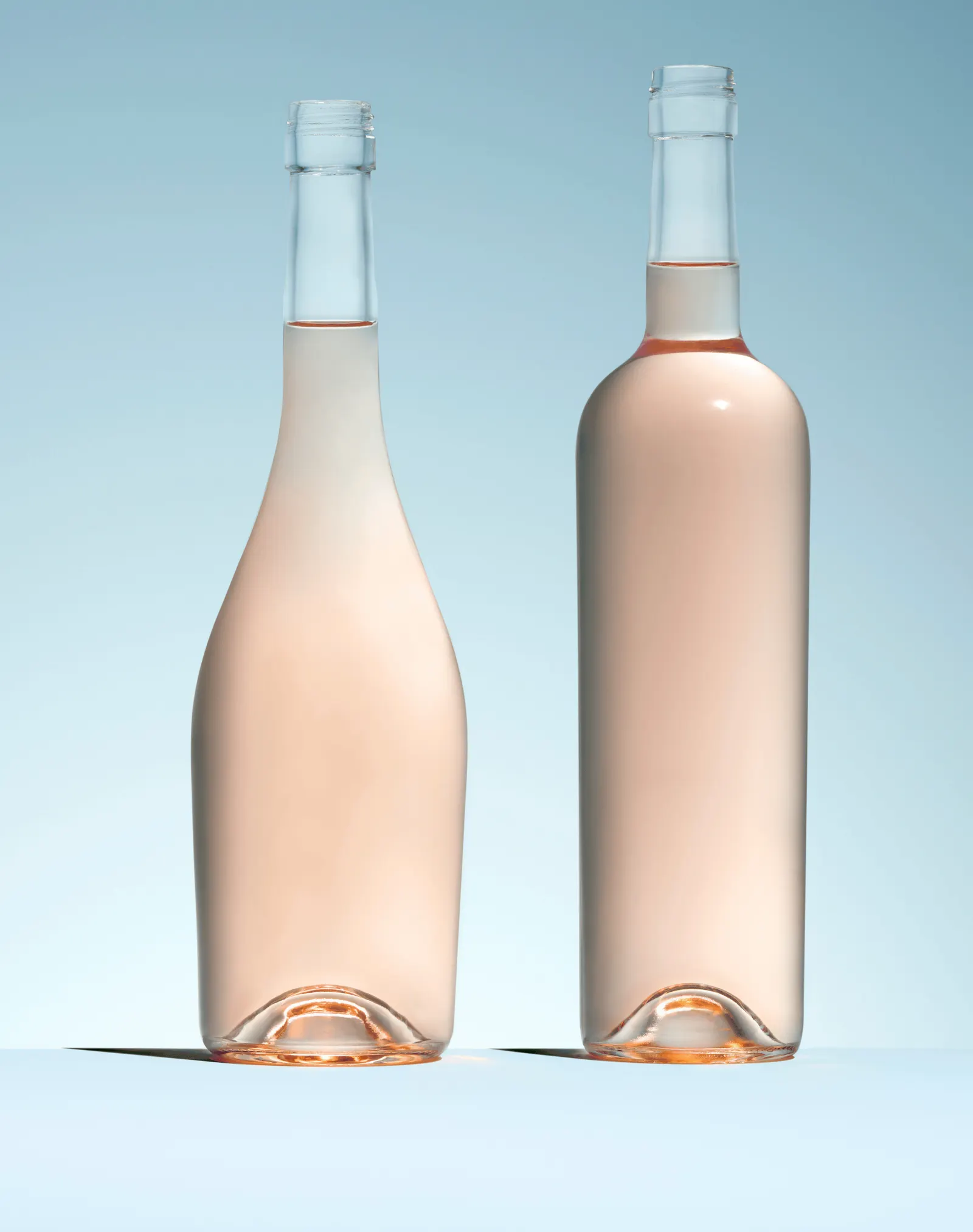 Two different shaped glass bottles filled with a pink wine.