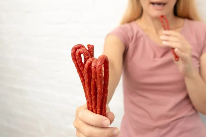 Person holding several meat sticks, about to eat one. Their face is partially visible, suggesting enjoyment or savoring the snack