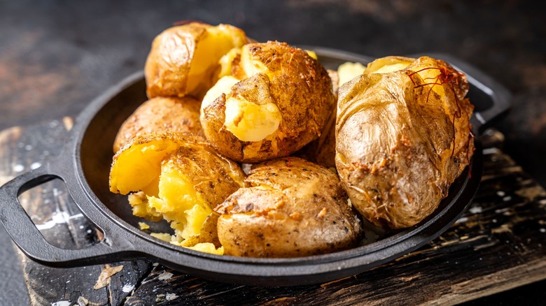 Crispy baked potatoes in a cast iron pan on a wood board