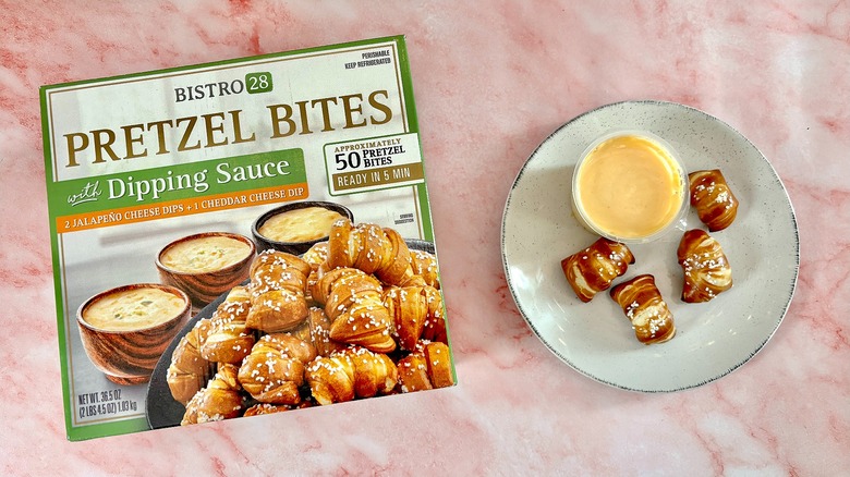 Bistro 28 pretzel bites and cheese cup on white plate next to box, on pink marble surface