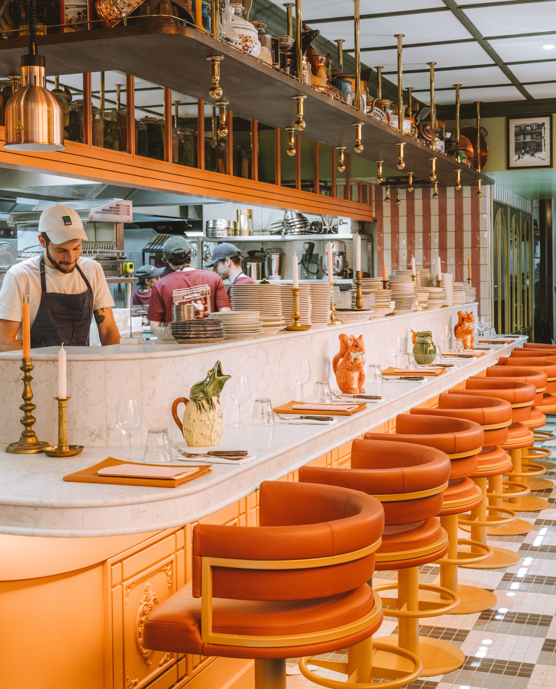 A row of fancy swivel stools along a long white chef’s counter looking into an open kitchen.