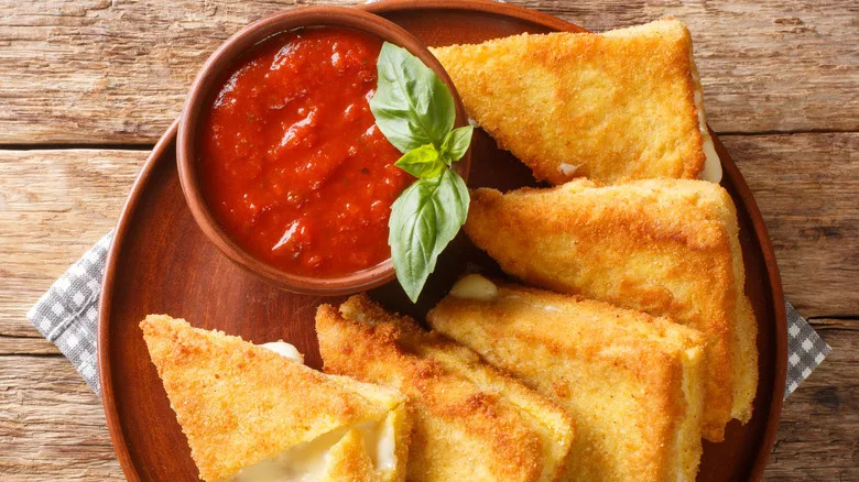 Mozzarella in carrozza on a wood plate with marinara dipping sauce and basil leaves