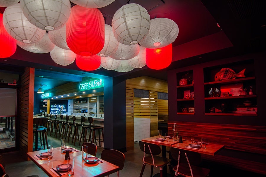 A Japanese restaurant is decorated with red and white paper lanterns and blue neon signage reads 