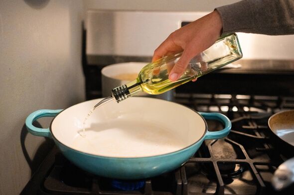 This is a close up photograph of a Hispanic man's hand pouring olive oil into a pan while cooking dinner at home in NYC.