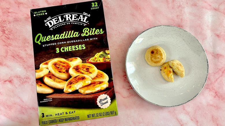Del Real Quesadilla Bites on white plate next to box, on pink marble surface