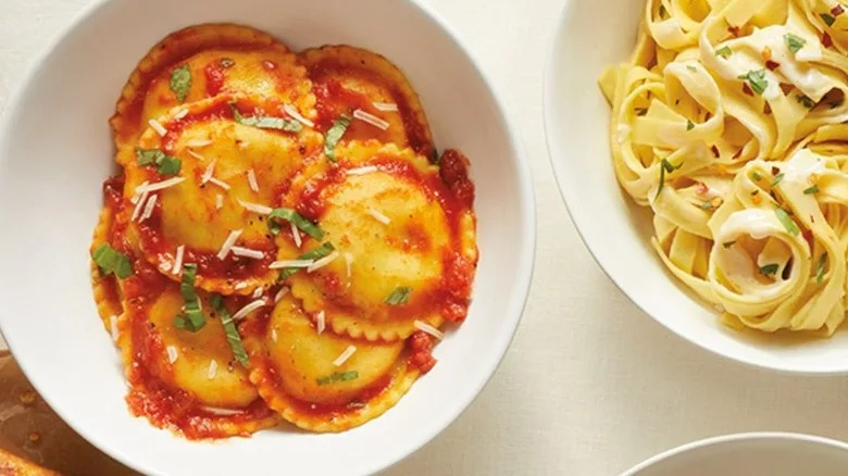 Aldi ravioli with tomato sauce, shredded cheese, and greens next to bowl of pasta