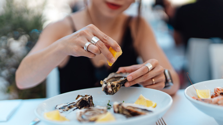 Mid-section of woman putting lemon on an oyster at a restaurant in France