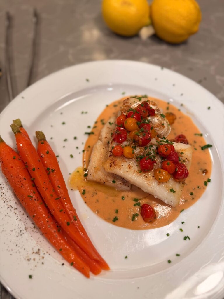 Pan seared fresh cod, sauce ivoire suprême, roasted pearl tomatoes, carrots glacé, chives, lemon, with jasmine rice served on the side.