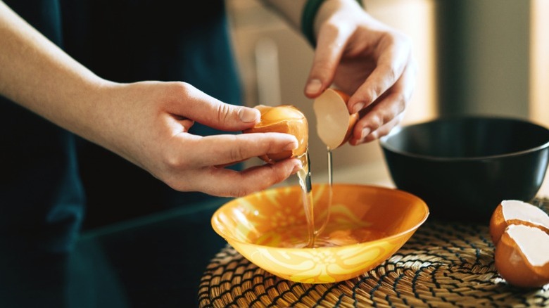 A girl in a kitchen cracking an egg into a bowl.