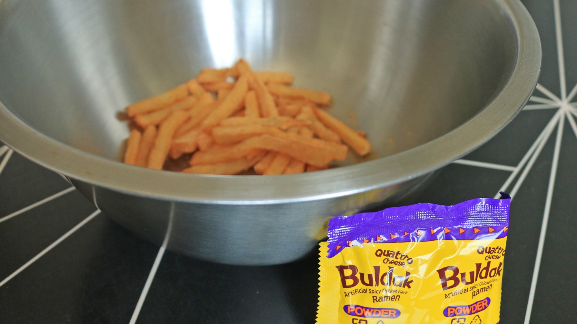A small packet of Buldak cheese seasoning in front of a bowl of french fries.