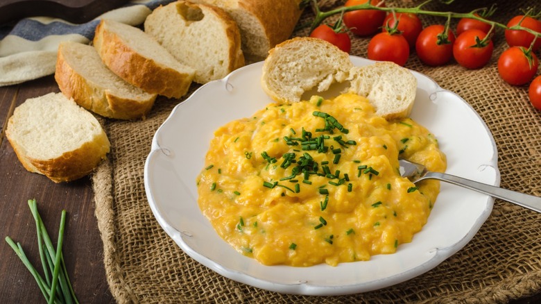 French-style scrambled eggs in a bowl next to sliced French bread.