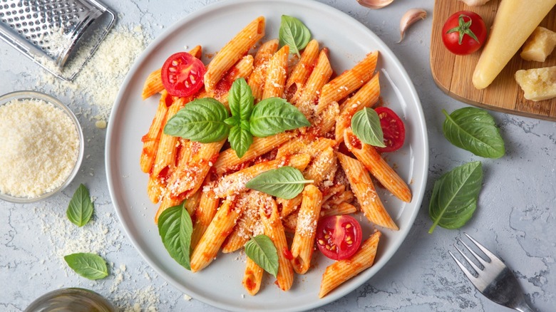 A pasta dish at an Italian restaurant with basil leaves and a side of parmesan