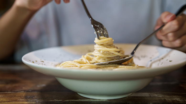 Person twirling pasta with a fork and spoon