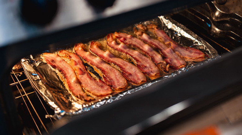 A foil-wrapped baking sheet with pieces of bacon laid on it in the oven