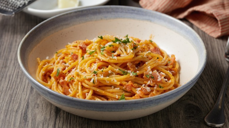 Spaghetti in a white bowl with a light blue rim on a wood table