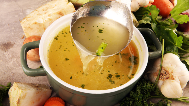 A cup of stock surrounded by veggies and garlic.