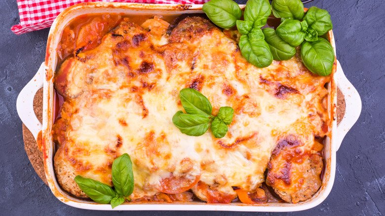 Overhead shot of eggplant in a casserole dish with melted cheese and fresh basil leaves