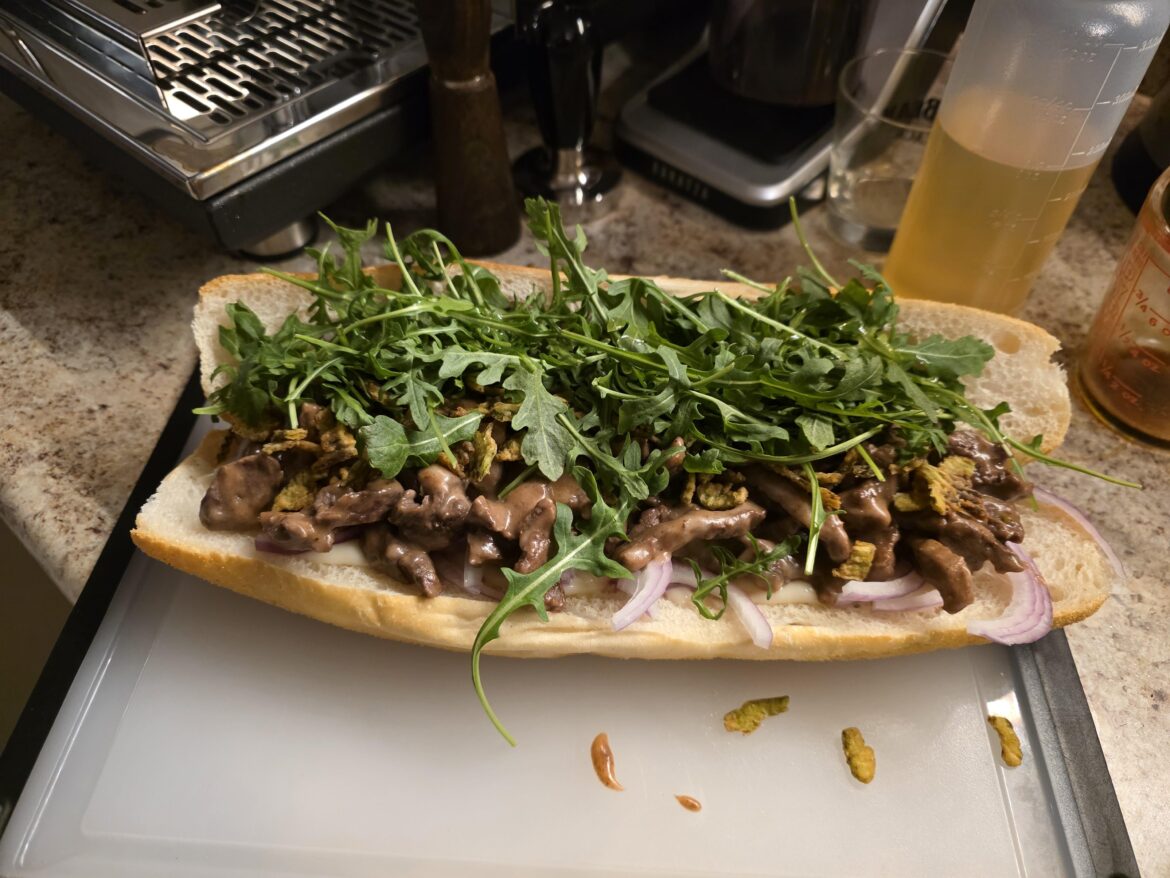 Cheesy steak sandwich w/ horseradish sauce, red onion, crispy jalapenos and baby arugula.